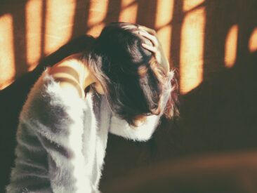 woman leans on wall in white fur jacket docking her head while holding it using her leaf hand