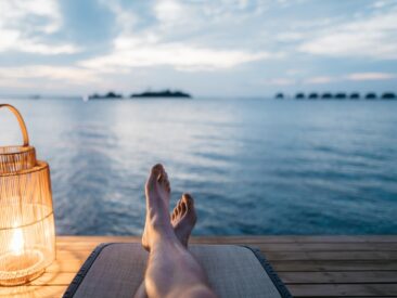 person lying on chair and facing on body of water